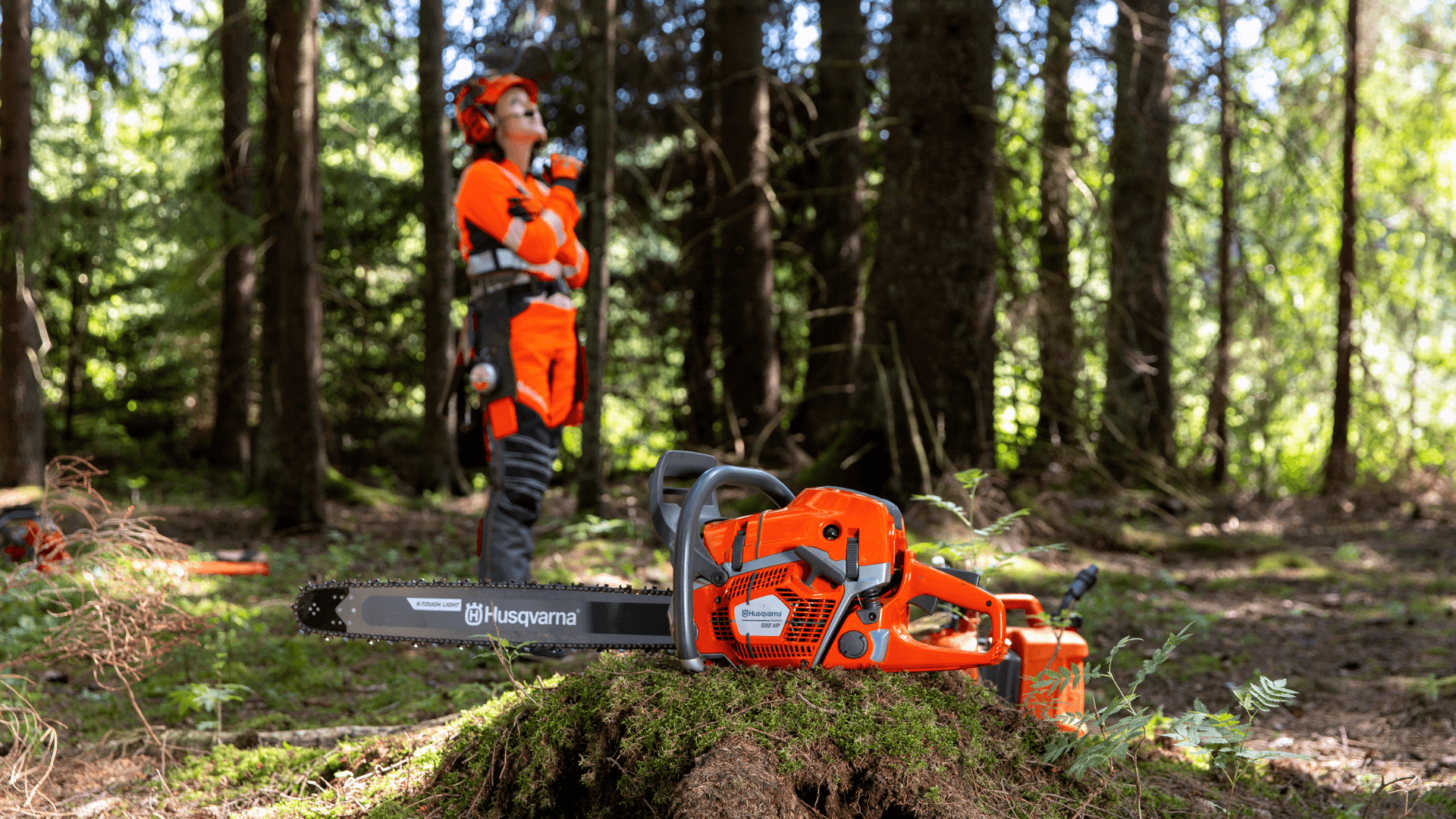 woman wearing protective gear in forest with chainsaw at front